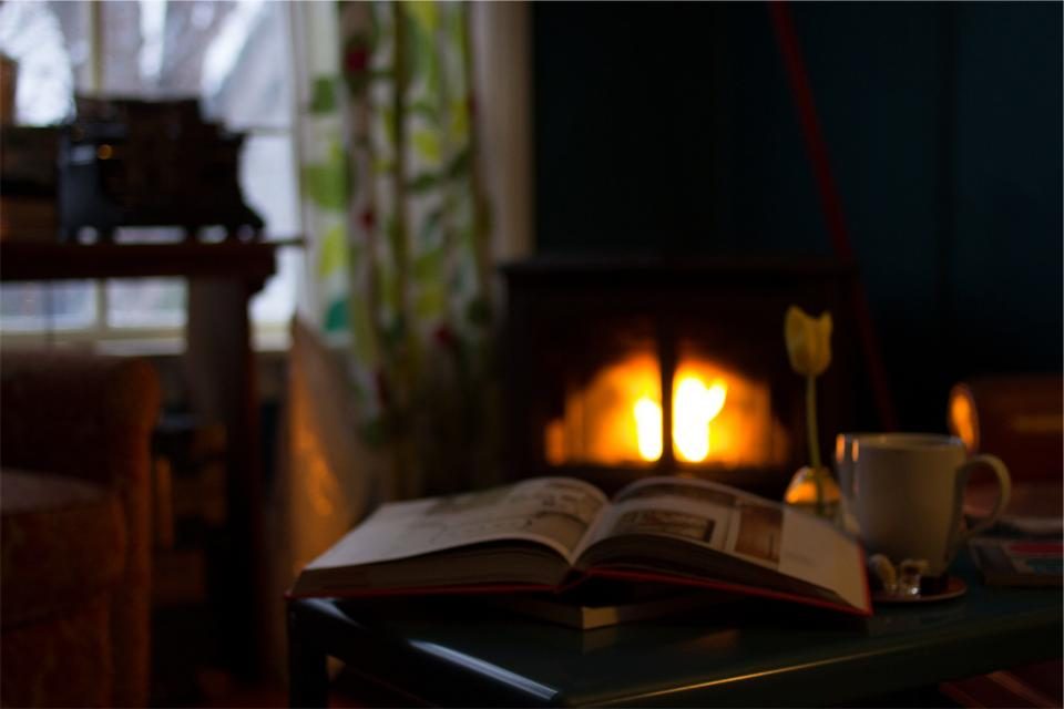 An open book and a cup of tea beside a glowing fireplace